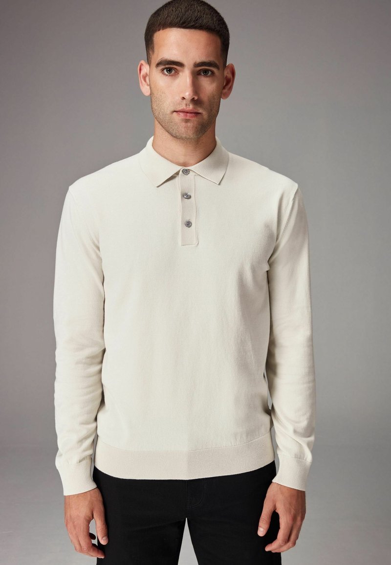 Suéter de polo de color crema claro con mangas largas, tapeta de tres botones, puños y dobladillo acanalados, fabricado en una suave tela texturizada.