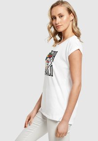 Hvid bomulds t-shirt med oprullede ærmer, prydet med en farverig Day of the Dead kranium grafik og sort tekst. Glat tekstur, afslappet pasform.