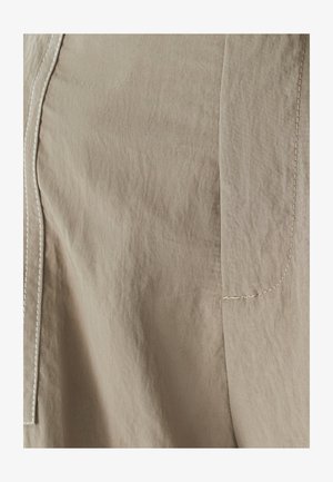 Pogled z bližine na bež tkanino z vidnimi šivi ob robovih, ki poudarja teksturo in podrobnosti šivov na obleki.