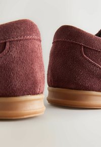 Burgundy suede shoes with a smooth rubber sole. The design features a rounded shape and stitching detail along the edges.