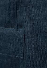 Mörkblått tyg med en strukturerad yta. Har synlig sömnad och en söm. Avslöjar delvis en fickdetalj.