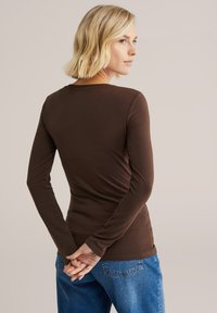 Barna hosszú ujjú ing, testhezálló szabással és lekerekített nyakkivágással, világoskék farmerral párosítva. Puha anyag, sima textúrával.