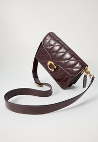 Quilted burgundy leather bag with a gold-tone clasp, adjustable strap, and a tag. Smooth texture with a classic rectangular shape.