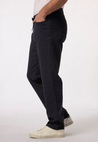 Granatowe spodnie z elastycznym paskiem, bocznymi kieszeniami i zwężanym krojem. Połączone z kremowymi trampkami na neutralnym tle.