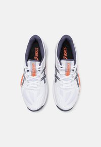 Baskets blanches de sport avec une tige en mesh texturé, accents orange, doublure intérieure marine et rayures noires. Présente un design à lacets et une semelle flexible.