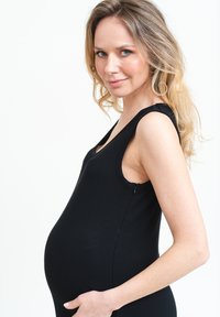 Czarny prążkowany top bez rękawów z szerokimi ramiączkami i suwakiem z boku, noszony przez kobietę z widocznym brzuchem ciążowym, na białym tle.