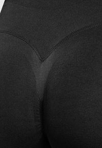 Leggings noirs en tissu lisse et extensible. Caractéristiques d'un design sans couture avec un détail en forme de V à l'arrière et une texture douce.