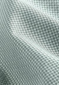 Textil texturat în verde deschis și alb cu un model în zigzag, având un design țesut care evidențiază adâncimea și dimensiunea.