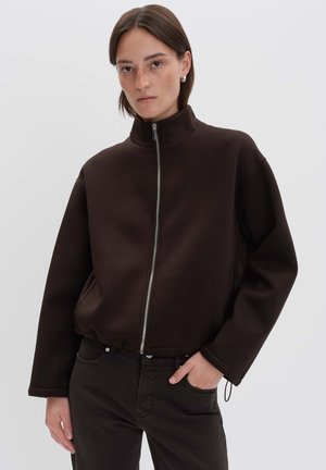 Bruine ritsjack gemaakt van gestructureerde stof met een hoge kraag, een relaxte pasvorm en zijzakken, gecombineerd met donkere broek.