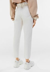 Pantalones de algodón blanco con mezclilla, con una cintura elástica, piernas ajustadas y bordes sin rematar en los puños, combinados con zapatillas blancas voluminosas.