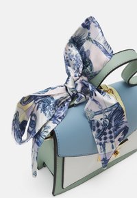 Borsa in pelle con schema di colori blu, verde e bianco, con una sciarpa di seta annodata in modo evidente sulla parte superiore, che mostra intricati motivi blu.