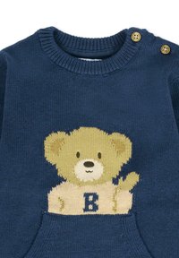 Niebieski sweter z dzianiny z beżowym wzorem misia, okrągłym dekoltem i dwoma złotymi guzikami na ramieniu. Miękka tekstura z kieszenią.