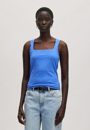 Blauwe tanktop met vierkante hals gemaakt van gladde stof, gecombineerd met lichtblauwe hoge taille jeans en een zwarte riem. Eenvoudig ontwerp zonder patronen.