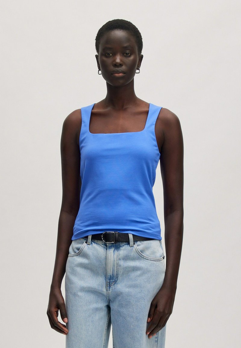 Blauwe tanktop met vierkante hals gemaakt van gladde stof, gecombineerd met lichtblauwe hoge taille jeans en een zwarte riem. Eenvoudig ontwerp zonder patronen.