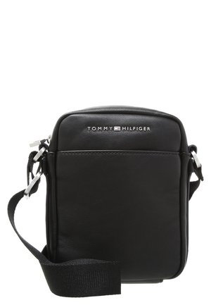 Sac bandoulière en cuir noir avec une sangle réglable et un logo Tommy Hilfiger argenté sur le devant.