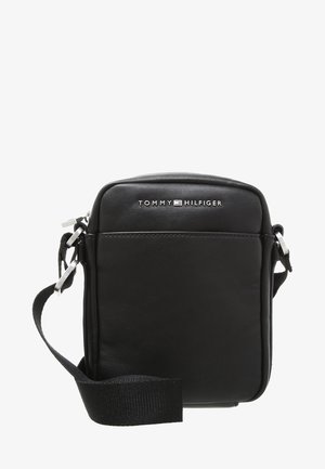 Sac bandoulière en cuir noir avec une sangle réglable et un logo Tommy Hilfiger argenté sur le devant.