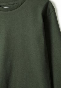 Maglietta a maniche lunghe verde scuro con collo a giro, realizzata in morbido tessuto a maglia, mostrata in primo piano su uno sfondo bianco.