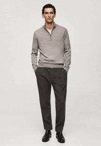 Harmaa, pitkähihaine pullover, jossa on vetoketjullinen kaulus, yhdistetty tummanharmaisiin laskostettuihin housuihin ja ruskeisiin nilkkabootseihin. Sileä rakenne, tiukka muotoilu.