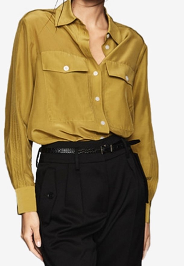 Chemise jaune moutarde à boutons avec deux poches avant, coupe ajustée et texture douce, portée avec un pantalon noir taille haute.