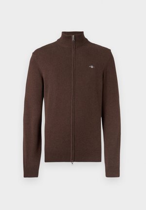 Maglione marrone con zip e collo alto, con polsini e orlo a coste. Tessuto morbido con un piccolo logo sul petto a sinistra.