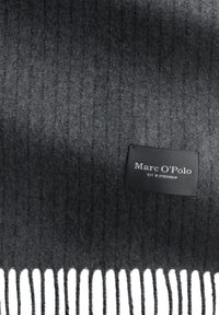Écharpe en laine côtelée gris foncé avec des franges blanches. Présente une étiquette noire avec le nom de la marque "Marc O'Polo" et "EST. À STOCKHOLM."