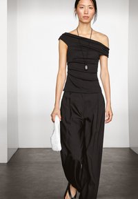 Zwarte off-shoulder top met geplooide textuur, losse zwarte broek en een witte gebreide tas. Eenvoudig ontwerp met minimale hardware en accenten.