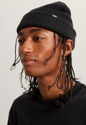 Svart ribbad stickad mössa med en liten Vans-logotyp, bärs av en person med långt, lockigt hår, i kombination med en svart sweatshirt.