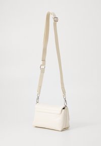 Bolso bandolera color crema con una textura suave de cuero sintético, forma rectangular, correa ajustable y herrajes en tono plateado.