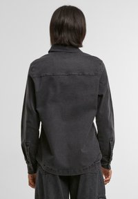 Zwarte denim shirt met een knoopsluiting kraag, lange mouwen en een ronde zoom; heeft gestikte details langs de naden.