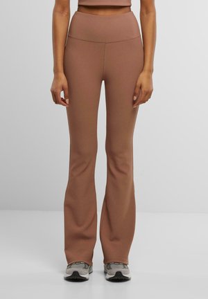 Leggings marron taille haute évasés en tissu extensible et texturé, ajustés en douceur au niveau des hanches, se terminant près de la cheville.