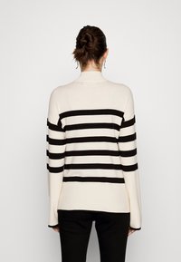 Krémový pletený svetr s černými horizontálními pruhy, s lichoběžníkovým límcem a dlouhými rukávy. Měkká textura a uvolněný střih se rovním lemem.