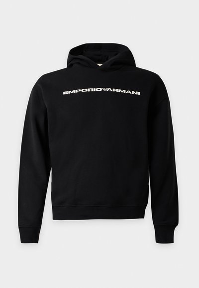 Μαύρο φούτερ Emporio Armani με κουκούλα και μακριά μανίκια, με λευκό λογότυπο στο στήθος σε γκρι φόντο.