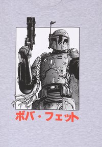 Grå t-shirt med en sort-hvid illustration af en figur i rustning, der holder en blaster, med rød tekst nedenfor på japanske tegn.