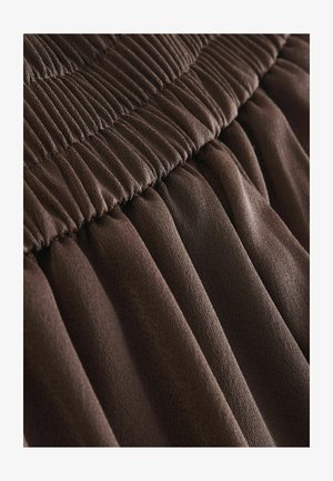 Prune tekstuuriga kangas, millel on voltimisdisain ja volditud vöökoht. Materjal tundub pehme ja veniv, tuues esile keerulised õmblusdetailid.