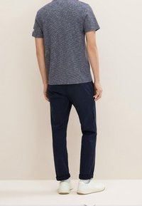 Pánské tričko s krátkým rukávem v námořnické heather barvě, spárované s námořnickými chinos kalhotami a bílými teniskami. Měkká textura, volný střih, detaily s ohrnutými manžetami.