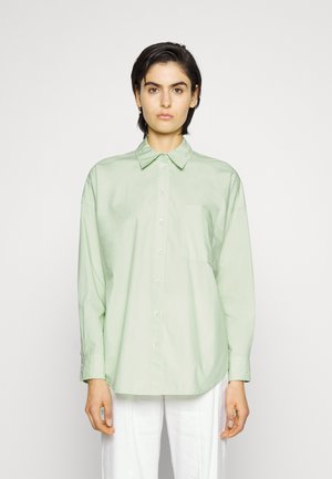 Jasnozielona koszula zapinana na guziki z kołnierzykiem, kieszenią na piersi i długimi rękawami. Wykonana z gładkiego materiału, w luźnym kroju, o minimalistycznym designie.