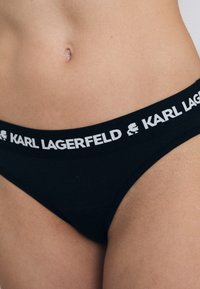 Slip bikini neri con banda bianca e logo "KARL LAGERFELD". Tessuto liscio con vestibilità aderente e design minimalista.