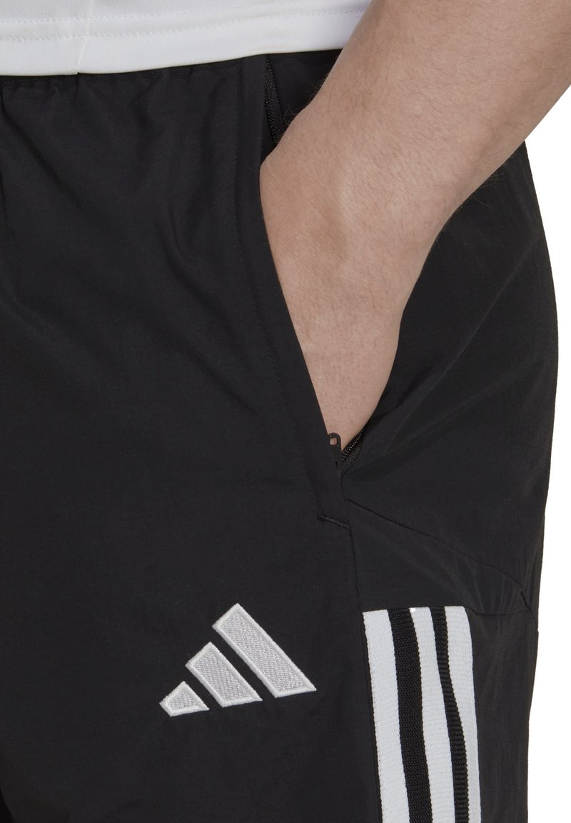 Pantaloni sportivi neri con tasca laterale, caratterizzati dal logo Adidas bianco e da tre strisce verticali in colori a contrasto. Tessuto leggero.