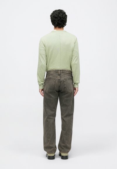 Light green long-sleeve shirt with a seam at the center back, paired with loose-fitting dark brown jeans and black shoes.
