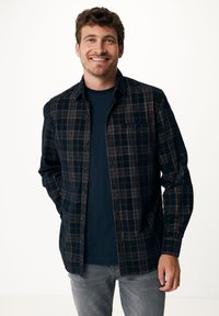 Camicia a quadri nera e arancione in morbido tessuto, con bottoni, dotata di taschino, indossata sopra una maglietta scura, abbinata a jeans grigi chiari.