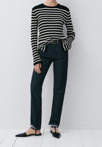 ZWART-WIT GESTREEPTE RIBBETEN TRUI SAMENGESTELD MET HOOGGEPLAATSTE DONKERE SPODEN, AFGEWERKT MET ZWARTE SPITSHAKEN EN EEN RRIEM.