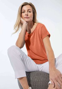 Rood-oranje korte mouwen top met een ronde halslijn, gecombineerd met lichtkleurige cropped broeken. Zachte textuur, losse pasvorm en eenvoudig ontwerp.