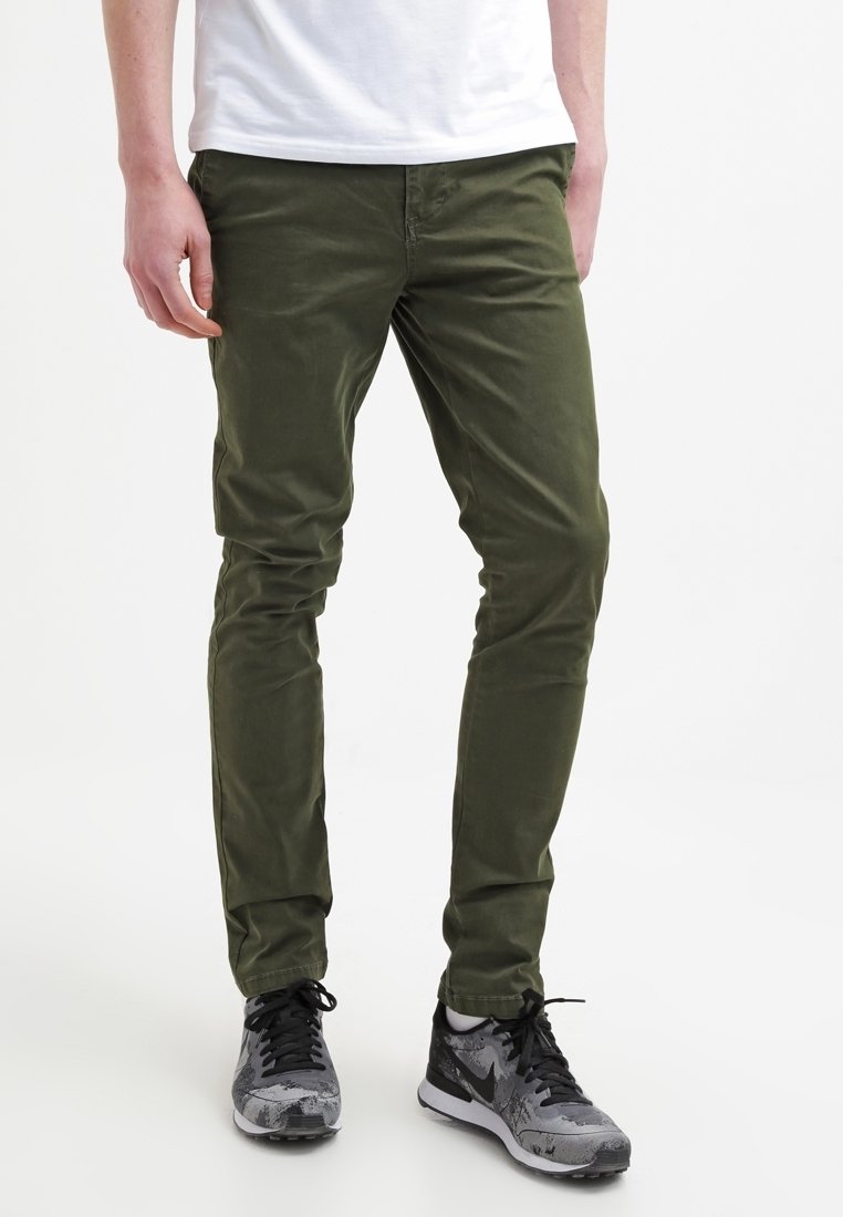 Olivgröna slim-fitbyxor i bomullstwill. Slät textur, femficksdesign, tillsammans med grå och svarta träningsskor.