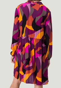 Robe colorée et fluide ornée de formes abstraites en violet, orange, rose et noir. Manches longues, col volanté et taille froncée.