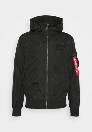 Sort zip-up bomberjakke med hætte, ribstrikkede manchetter, patch på brystet og en rød "Remove Before Flight"-mærkat på lynlåsen på venstre ærmelomme.