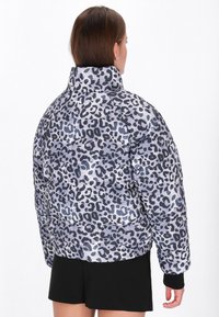 Magas nyakú, rugalmas szegéllyel ellátott puffernadrág, szürke és fekete leopárdmintával, világos háttéren.