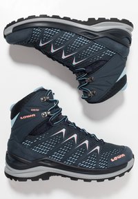Donkerblauwe wandelschoenen met gaasdetails, GORE-TEX materiaal, rubberen zool, grijze accenten en een roze logo. Beschikt over een hoge enkeldesign.