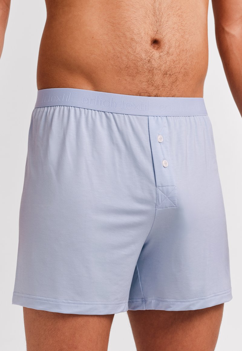 Lichtblauwe katoenen boxershorts met een zachte tailleband, twee knopen aan de voorkant en een vierkante patch op de achterkant voor een extra detail.