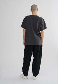 Gray oversized T-shirt with short sleeves, paired with black loose-fitting pants and white sneakers, featuring a relaxed design.