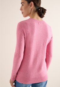Różowy sweter wykonany na drutach, z okrągłym dekoltem, żebrowanymi mankietami i dołem, charakteryzujący się gładką teksturą i luźnym krojem, w zestawie z dżinsami.